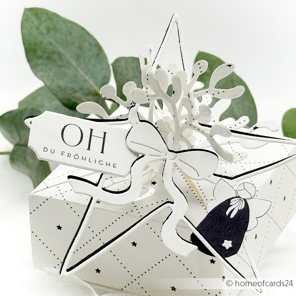 Weiße sternförmige Geschenkschachtel von Alexandra Renke, hergestellt mit Designpapieren und der Motivstanze Großer Stern, mit der Aufschrift "Oh du Fröhliche", verziert mit festlichem Dekor und Grünzeug im Hintergrund.