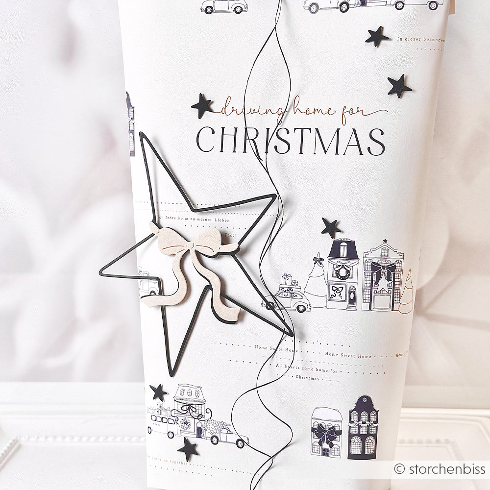 Das weiße Weihnachtsgeschenkpapier von Alexandra Renke zeigt schwarze Sterne, die von der Motivstanze Großer Stern inspiriert sind, sowie zarte Strichzeichnungen von Häusern und Autos für einen festlichen, modernen Look.