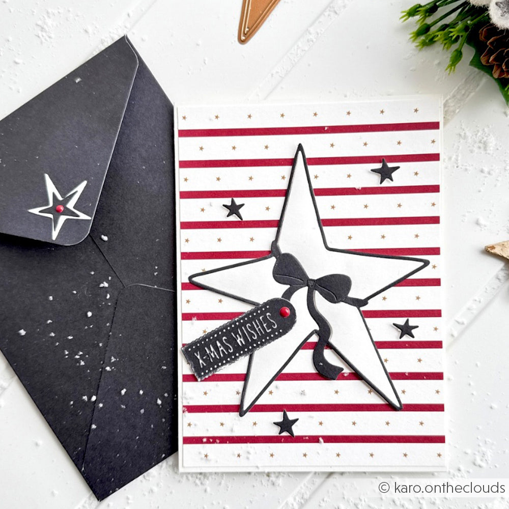 Weihnachtskarte von Alexandra Renke mit schwarzen und weißen Sternen aus der Motivstanze Großer Stern, einer Schleife, dem Anhänger XMAS WISHES und einem schwarzen Umschlag. Gefertigt aus hochwertigen Designpapieren 200g für eine elegante DieCut Systeme Veredelung.