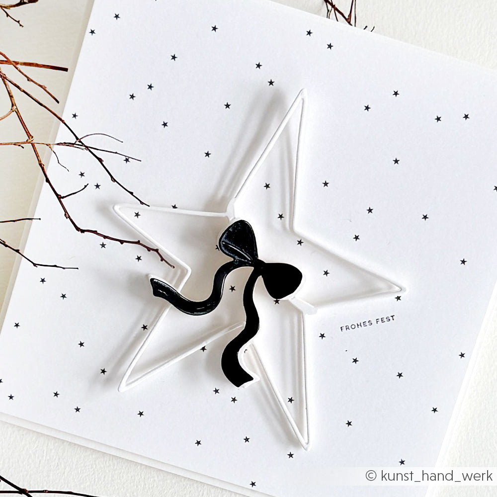 Minimalistische Weihnachtskarte von Alexandra Renke mit einem weißen 3D-Stern aus der Motivstanze Großer Stern, akzentuiert durch eine schwarze Schleife und kleine schwarze Sterne auf strahlend weißem Designpapier.