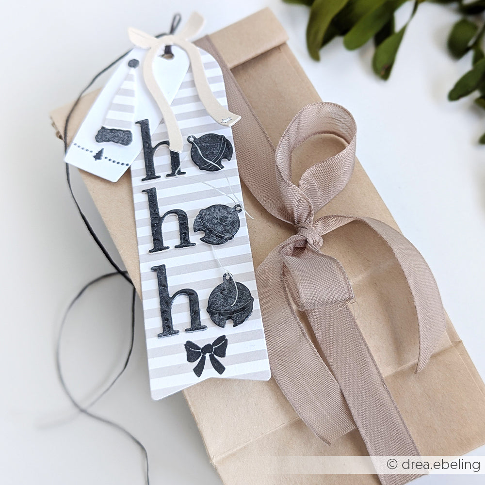 Geschenktüte von Alexandra Renke mit beigem Band und gestreiftem "ho ho ho"-Anhänger, verziert mit Teekannen und einer Schleife - ideal, um Ihre Designpapiere zu präsentieren oder mit DieCut Systemen für kreative Verpackungen zu kombinieren.