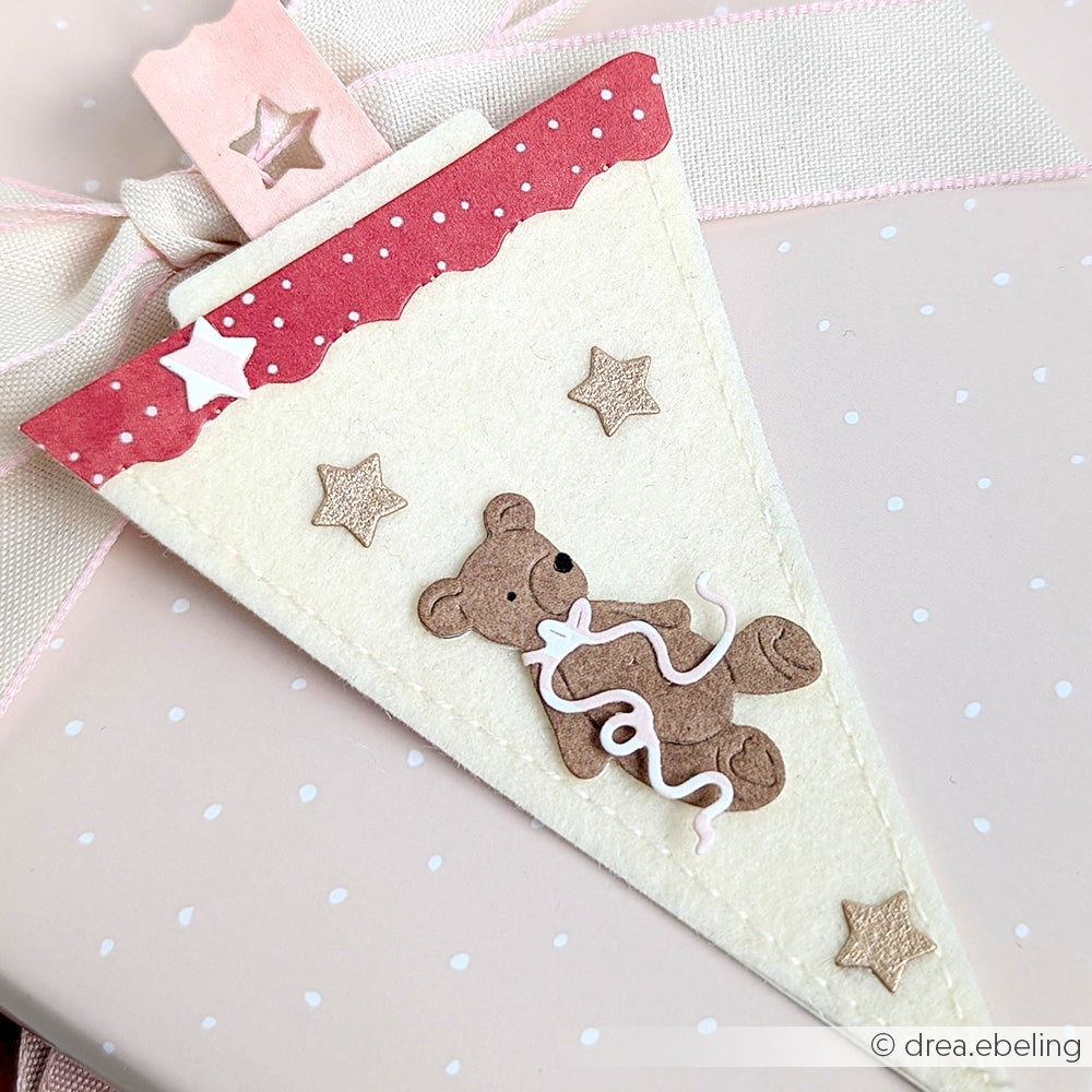 Ein Wimpel aus Filz mit Teddybär, Sternen und Schleife ziert eine zartrosa gepunktete Geschenkbox - perfekt für Spielzeugfreunde und handwerklich gefertigt aus charmanten Designpapieren von Alexandra Renke.