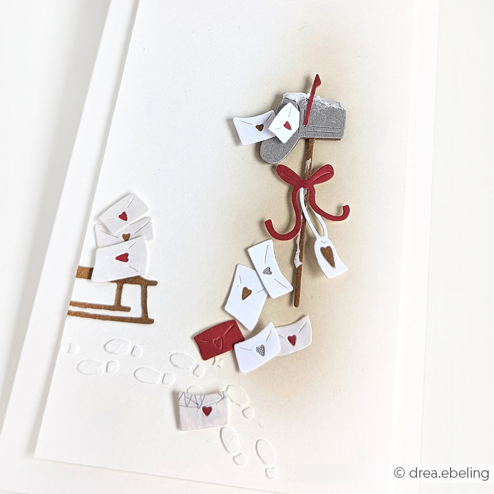 Ein Briefkasten voller Briefe, roter Schleife, Postweg und verschneiter Fußabdrücke - ideal zum Basteln mit Alexandra Renke Designpapieren oder zum Verzieren mit Motivstanze Herzenspost und Stanzen.