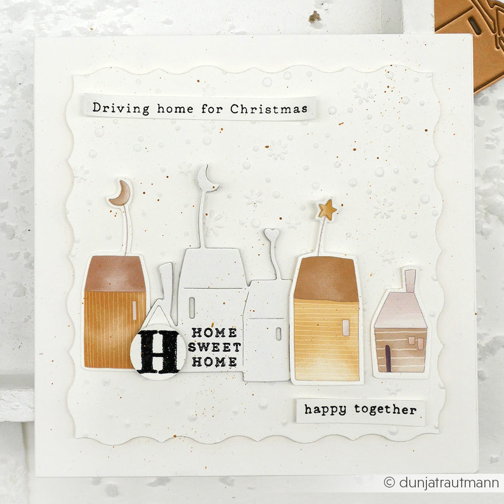 Eine handgefertigte Karte von Alexandra Renke mit illustrierten Häusern, Schneeflocken und dem Text "Driving home for Christmas and happy together" - hergestellt mit ihren Designpapieren und Mondhäuser DieCut Systemen.