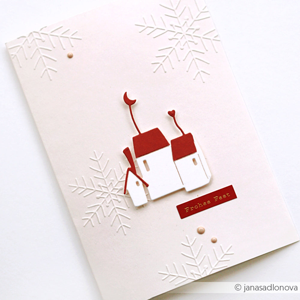 Minimalistische Weihnachtskarte von Alexandra Renke mit geprägten Schneeflocken und roten Dächern mit der Aufschrift "Frohes Fest". Mit einzigartigen festlichen Details, die mit der Motivstanze Mondhäuser gefertigt wurden.