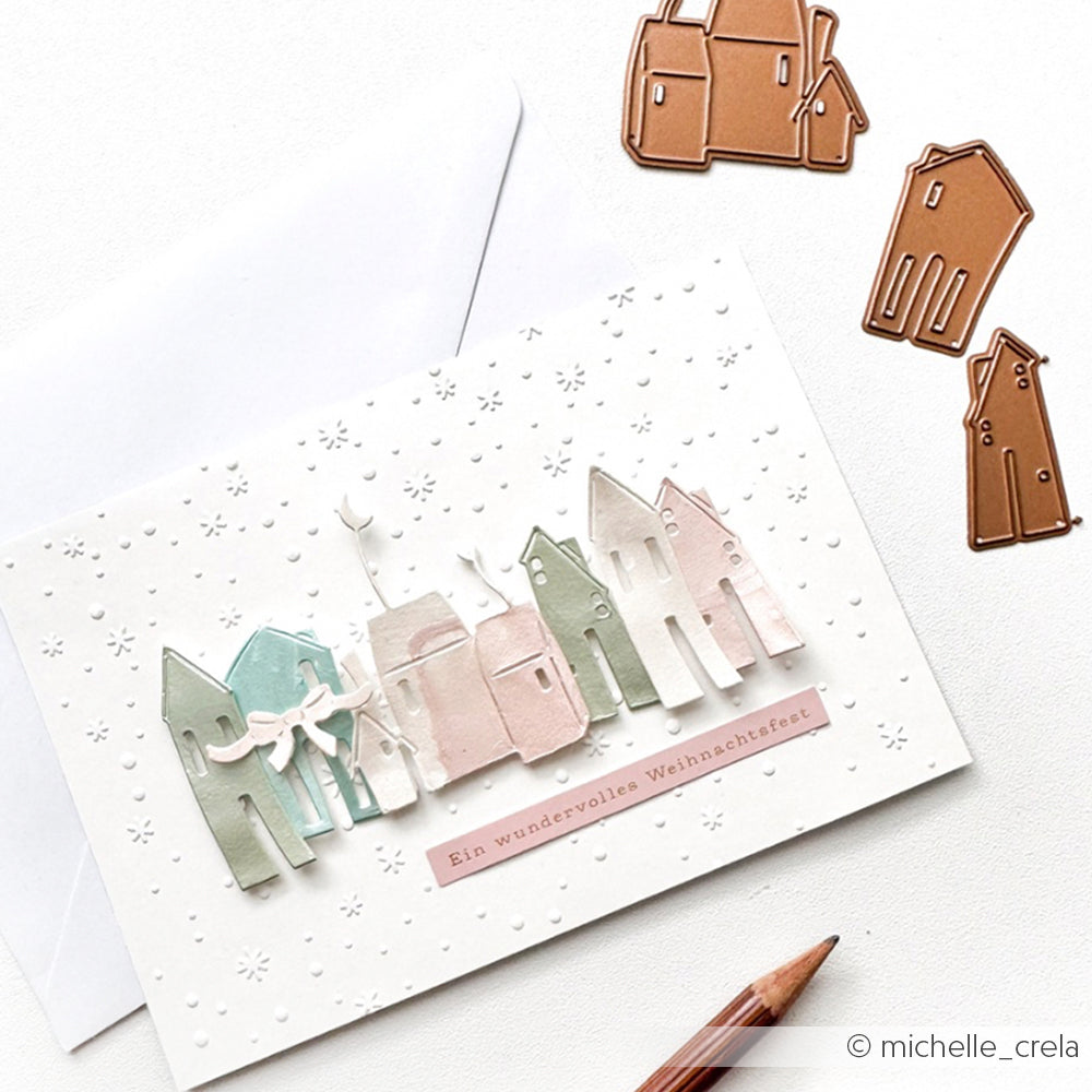 Handgemachte Weihnachtskarte mit pastellfarbenen Häusern aus Alexandra Renke Designpapieren und einem geprägten weißen Hintergrund, dargestellt mit Metallhäuschen - ideal für DieCut Systeme wie die Motivstanze Mondhäuser.