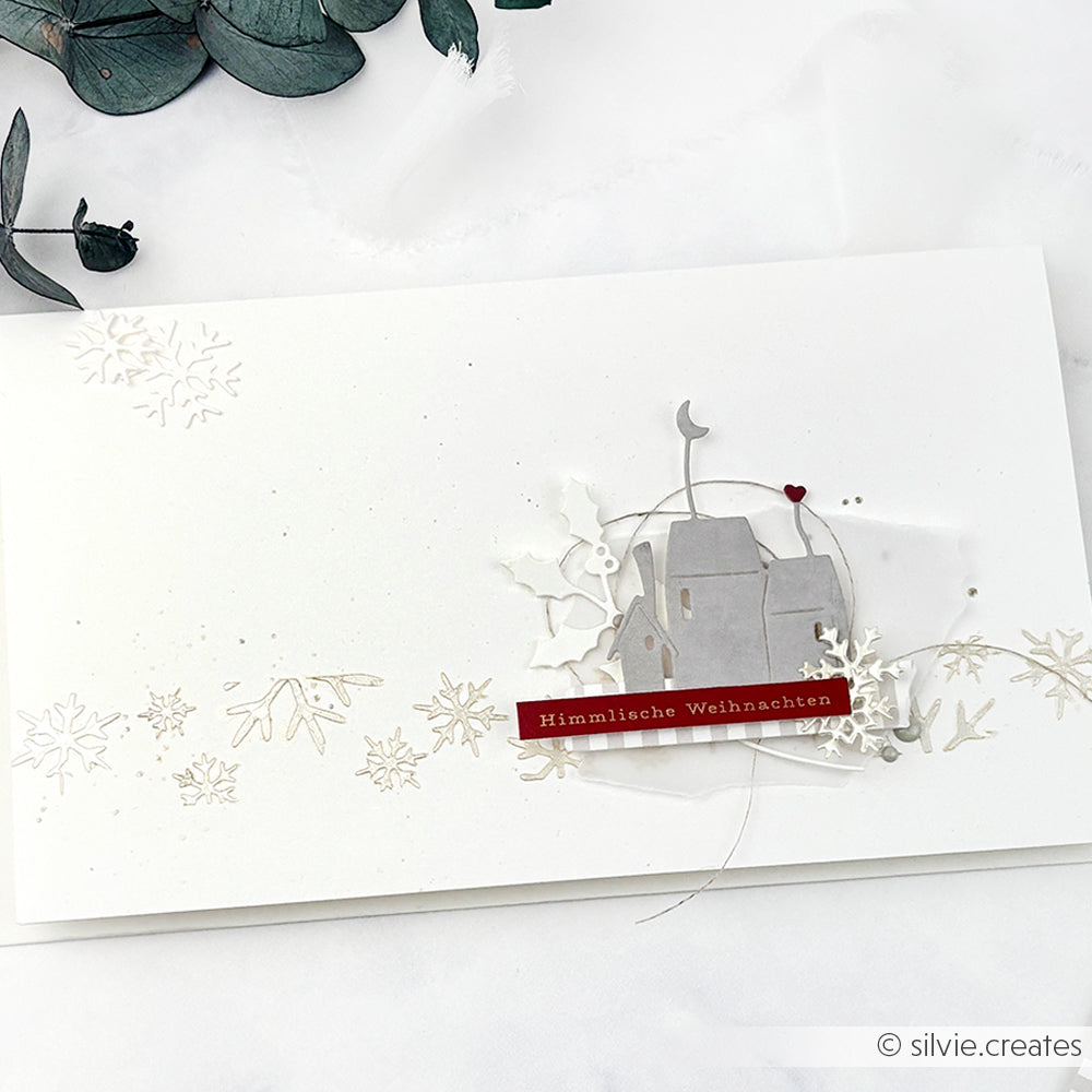 Minimalistische Weihnachtskarte von Alexandra Renke mit Schneeflocken, einem kleinen Haus und "Himmlische Weihnachten" auf einem roten Etikett, hergestellt mit der Motivstanze Mondhäuser für zusätzliche Details.