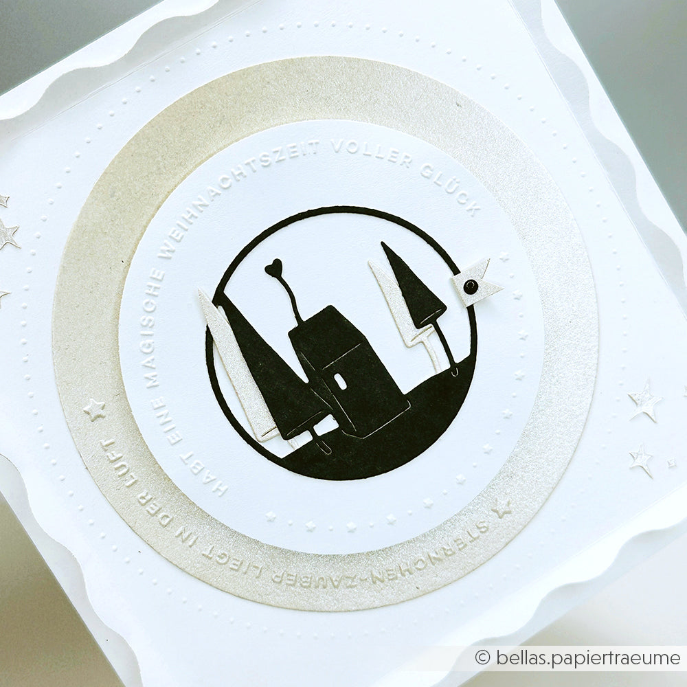 Weiße Weihnachtskarte von Alexandra Renke mit einem silbernen Kreis, einem abstrakten schwarzen Haus und Bäumen sowie einem deutschen Festtagstext in einem Ring, der mit der Motivstanze Herzhaus gestaltet wurde.