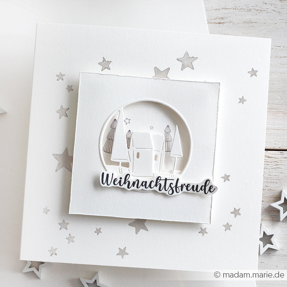 Weiße Weihnachtskarte von Alexandra Renke mit einer 3D-Dorfszene mit Herzhaus-Motivstempel und Stanzsystemen, deutschem Text, silbernen Sternen und hochwertigem Designpapier.