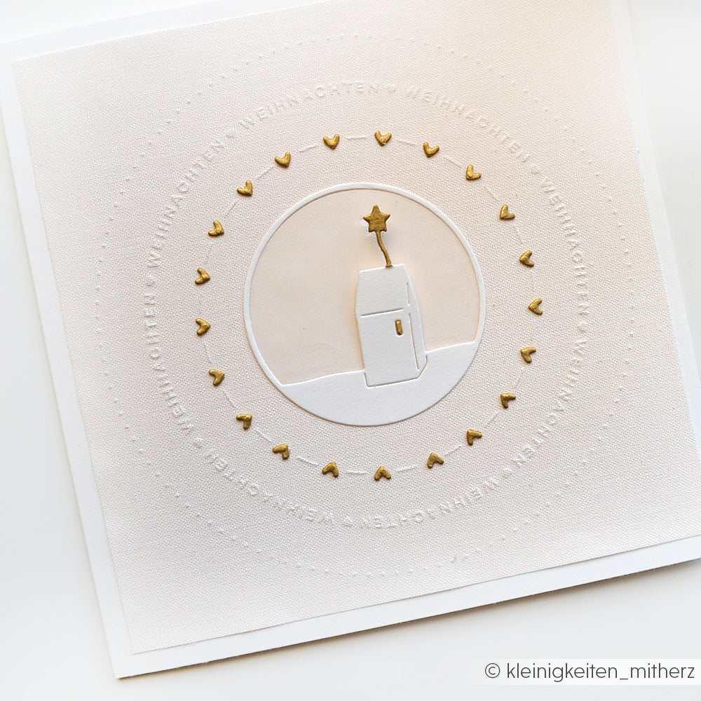 Minimalistische Weihnachtskarte von Alexandra Renke auf weißem Strukturpapier, mit goldenen Herzen, die ein weißes Haus und einen Stern umkreisen, hergestellt mit dem Sternenhaus-Stanzsystem.