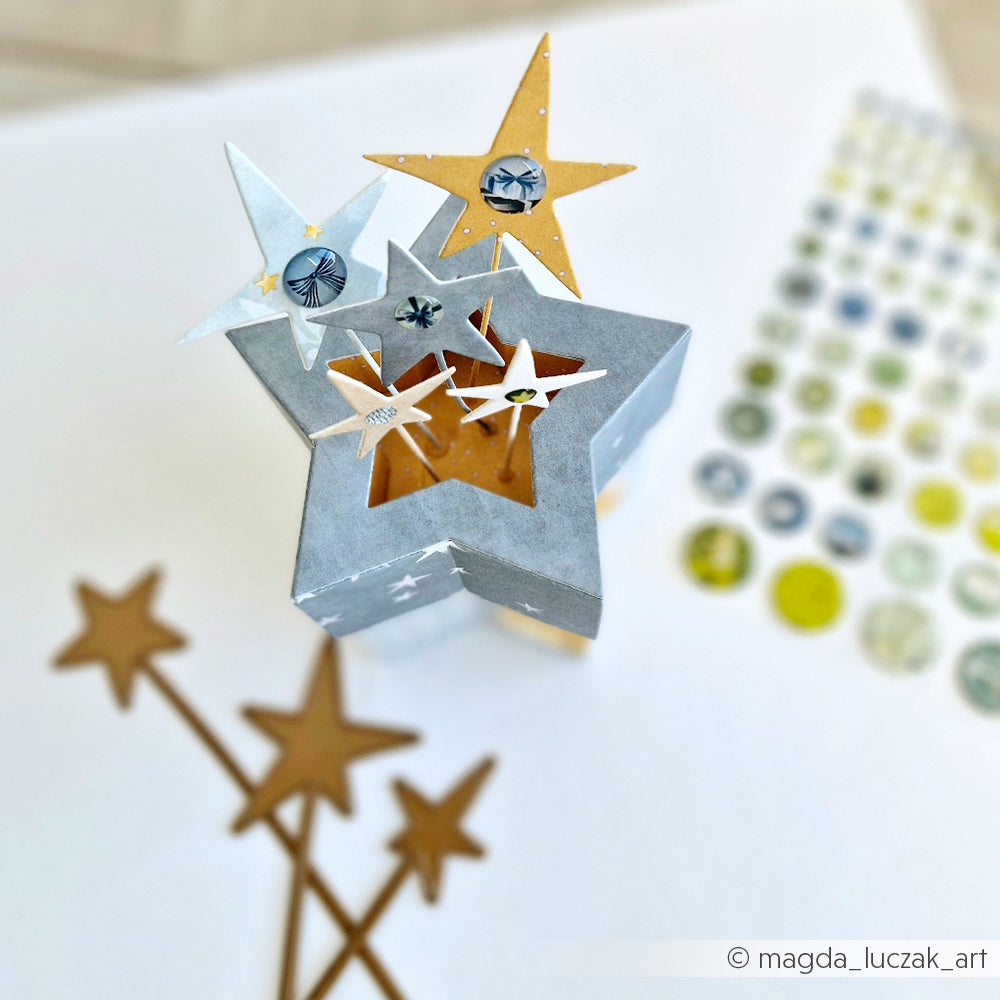 Sternförmige Box mit verzierten Sternenstäben und Bastelstickern auf weißer Oberfläche, mit Alexandra Renke Motivstanze Sterne und leuchtenden Designpapieren für kreatives Flair.
