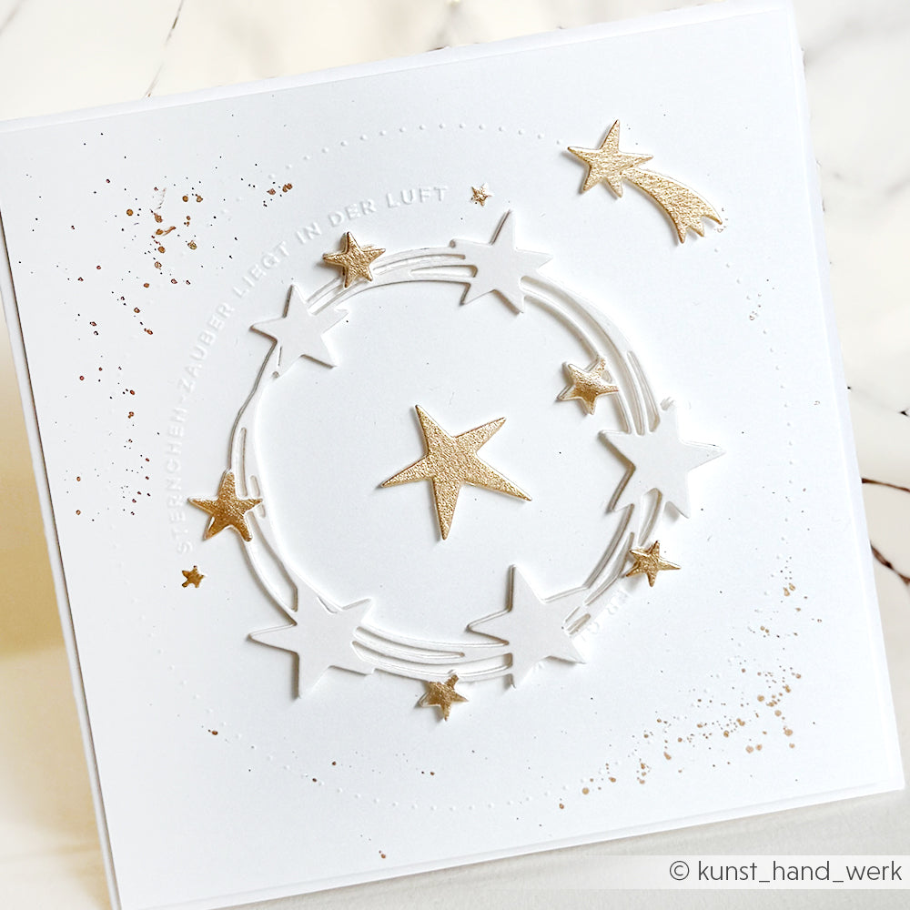 Weiße Karte mit goldenen und weißen Sternen, Spritzern und geprägtem deutschen Text in einem kreisförmigen Design, hergestellt mit Alexandra Renke Designpapieren und der Motivstanze Fröhlicher Sternenkranz für einen festlichen Touch.
