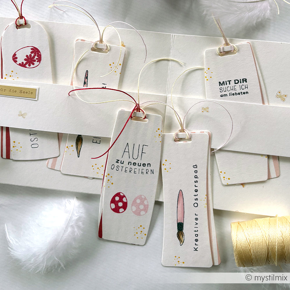 Handgefertigte Oster-Lesezeichen von Alexandra Renke mit deutschem Text, Kordelzug, weißen Federn, einzigartigen Formen aus Motivstanze Bauchiges Etikett und eleganten Akzenten aus Designpapieren.