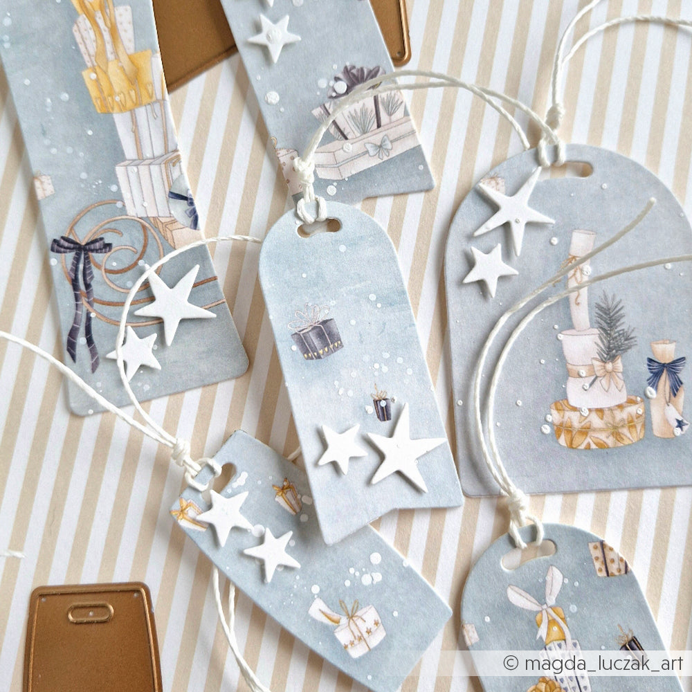 Mit Alexandra Renke Motivstanze Etiketten Trio und Designpapier gestaltete Geschenkanhänger mit blauen und goldenen Geschenkmotiven, weißen Sternverzierungen und weißen Schnüren auf gestreiftem Hintergrund.