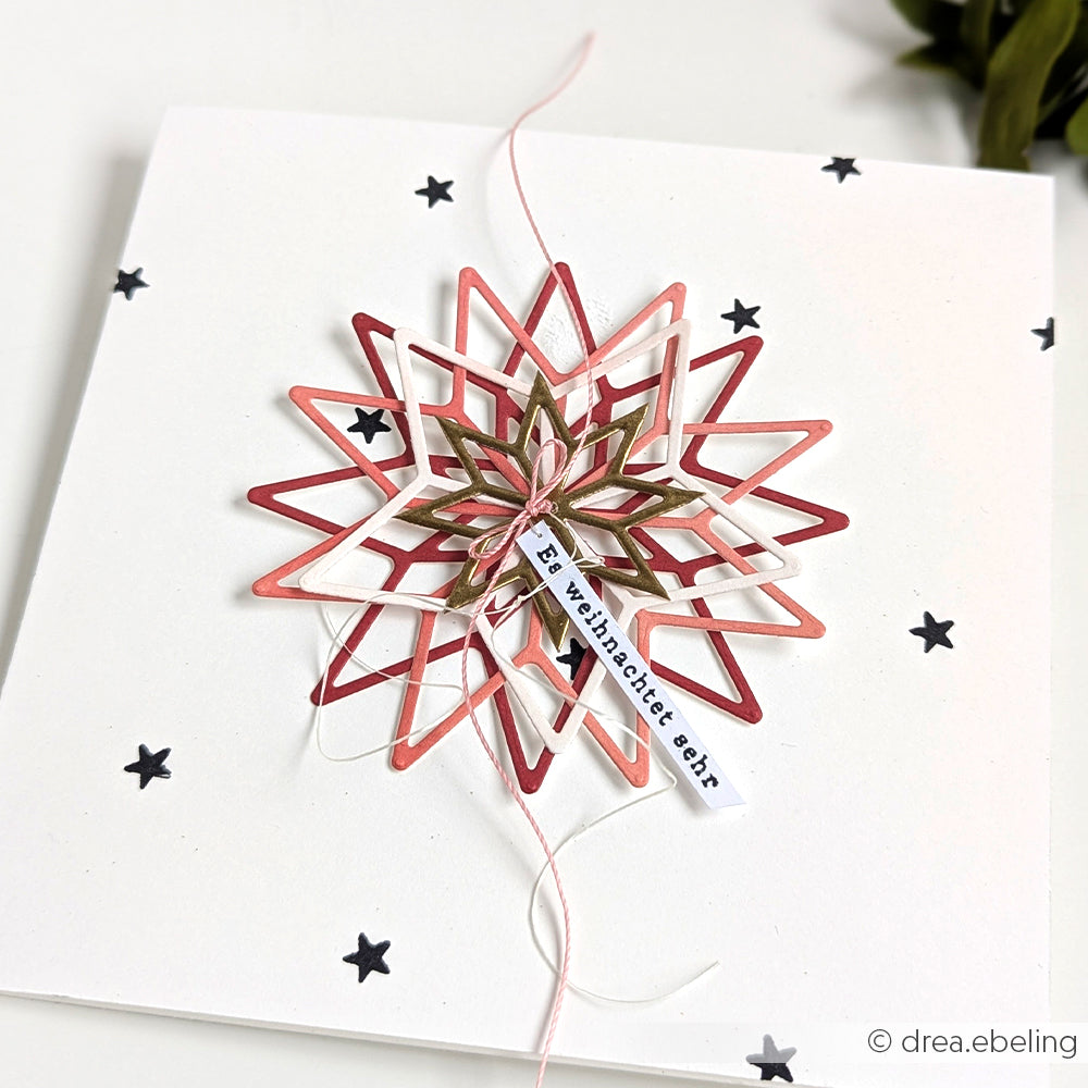 Handgefertigte Karte von Alexandra Renke mit Motivstanze Stern und DieCut Systemen, einem kleinen Anhänger mit der Aufschrift "Frohe Weihnachten euch" und schwarzen Sternen auf weißem Grund.