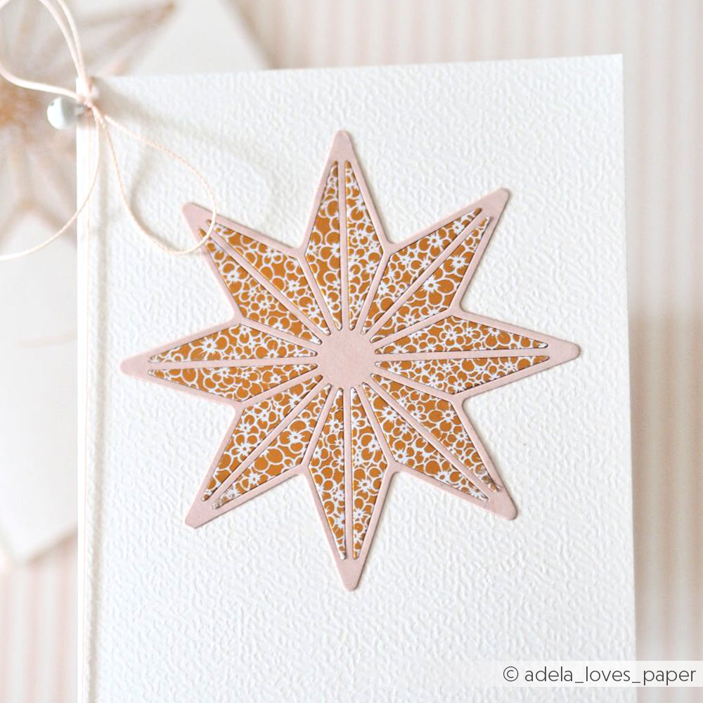 Eine strukturierte Karte von Alexandra Renke zeigt einen achtzackigen Stern in Rosa und Gold, der auf der Vorderseite mit dem Motivstanze Achterstern DieCut System präzise ausgeschnitten wurde.
