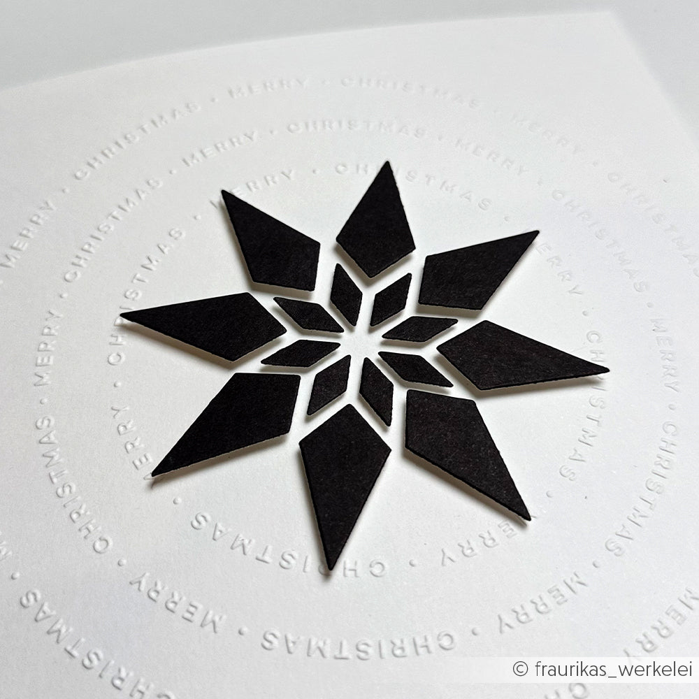 Schwarze geometrische Schneeflocke auf weißem Papier mit geprägtem Text Frohe Weihnachten, erstellt mit der Alexandra Renke Motivstanze Achterstern für präzise Schnitte und elegante Designpapiere.