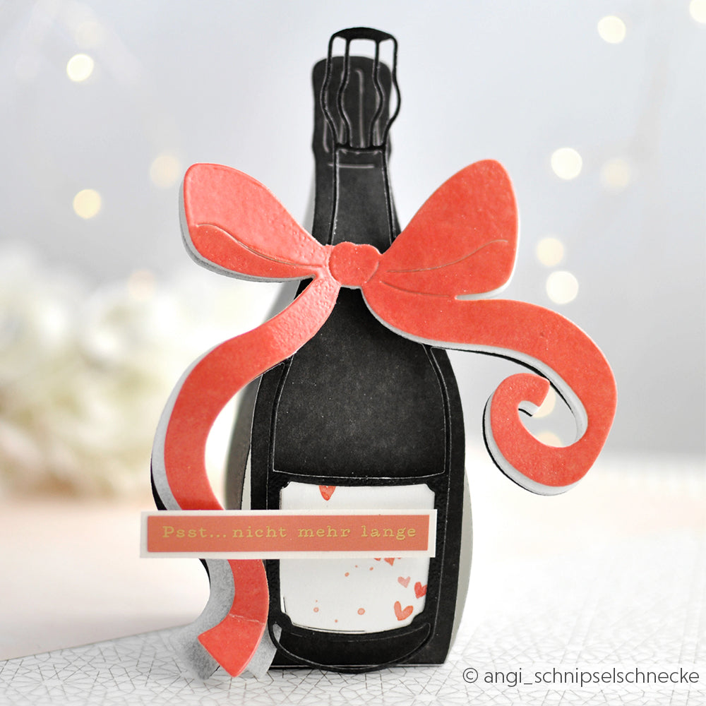 Eine Champagnerflaschenkarte von Alexandra Renke Designpapiere, verziert mit einer großen roten Schleife und dem Schriftzug "Psst... nicht mehr lange", ist mit der Motivstanze Champagnerflasche Stanzsysteme gestaltet.