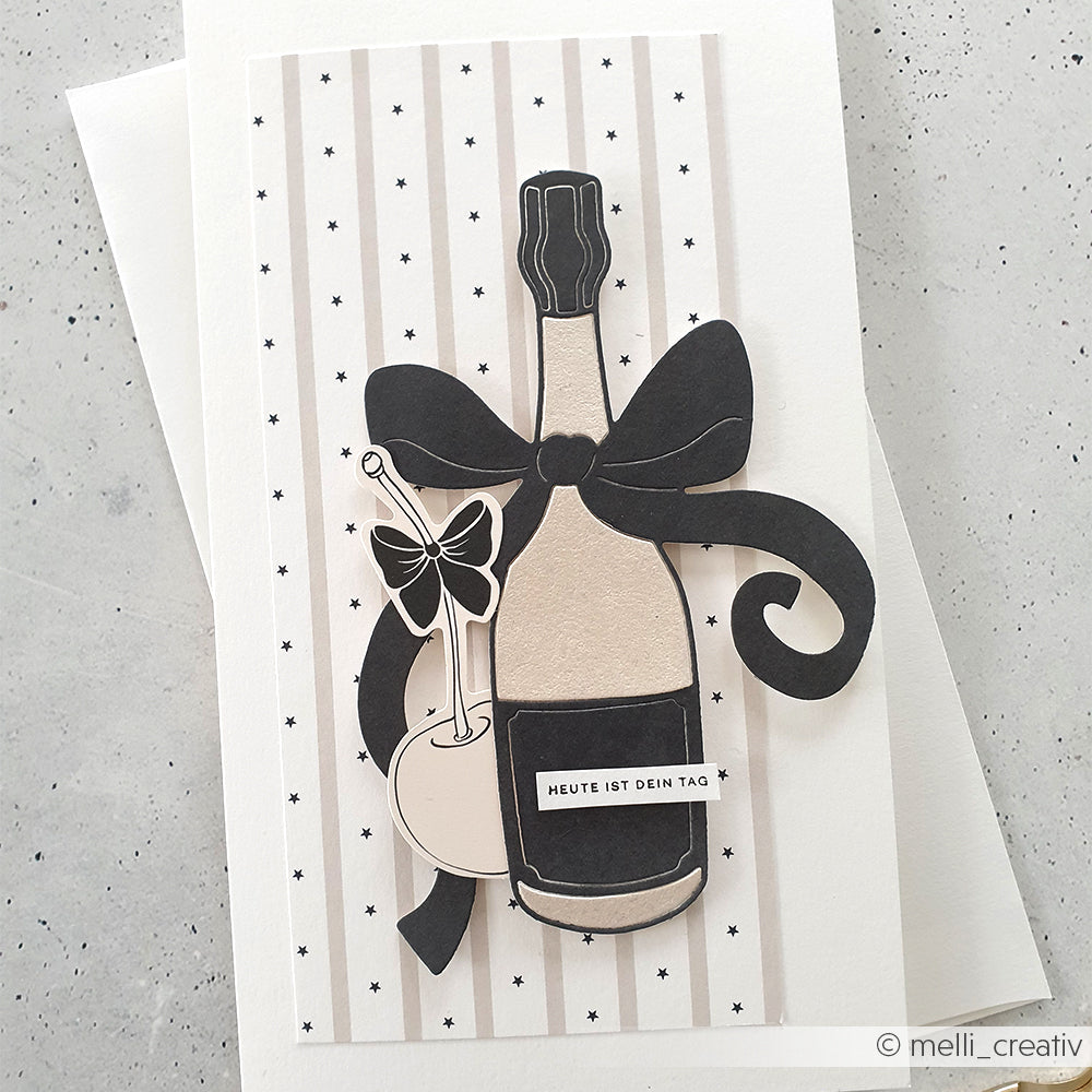 Grußkarte von Alexandra Renke mit einer großen Sektflasche, einer Schleife und Gläsern auf gestreiftem Hintergrund mit schwarzen Sternen - ideal, um besondere Momente mit kreativen Stanzungen für Designpapier zu feiern.