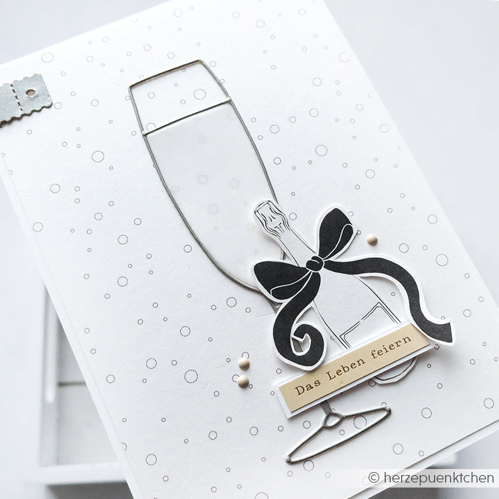 Minimalistische Karte von Alexandra Renke mit einer Sektglas-Stanzung, schwarzer Schleife und "Das Leben feiern". Ideal für Feiern mit eleganten Stanzen und einzigartigem Designpapier.