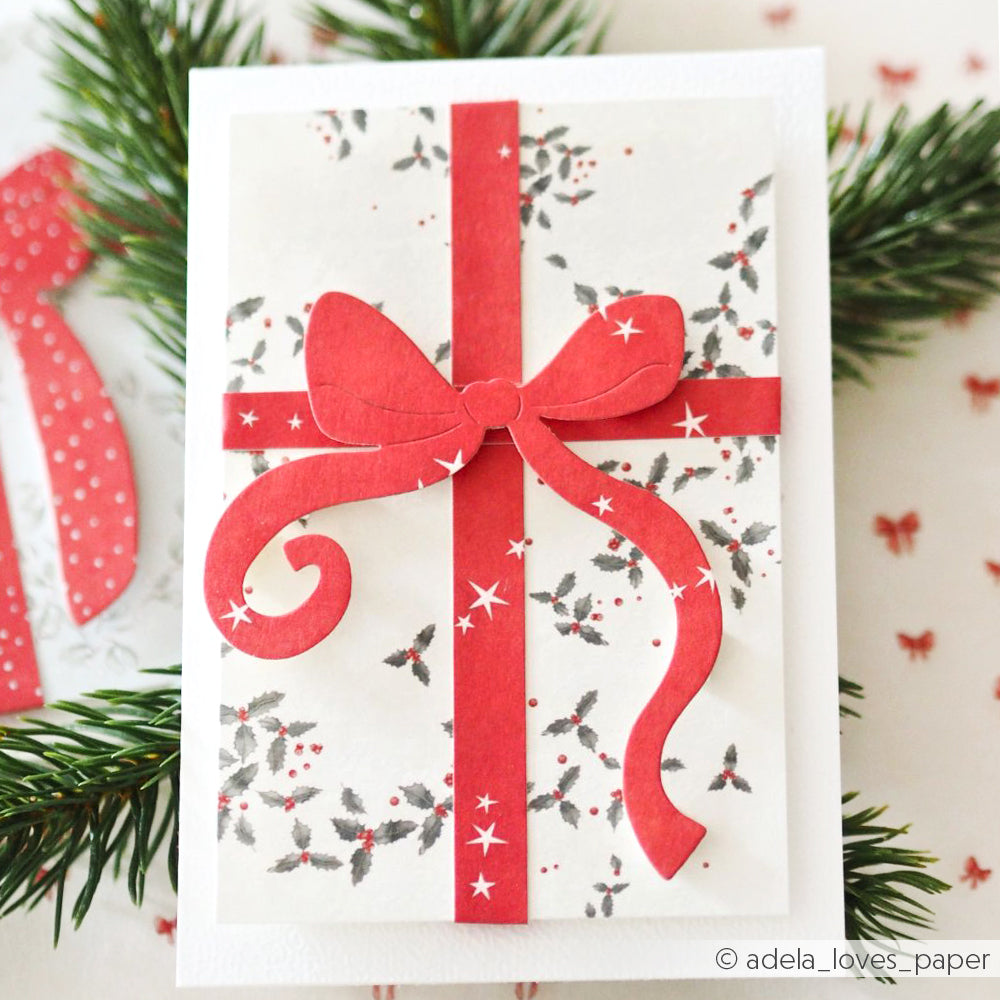 Handgefertigte Karte von Alexandra Renke mit roter Schleife und Band, gefertigt aus hochwertigen Designpapieren und veredelt mit der Motivstanze Festtagsschleife, die mit Stechpalmen- und Sternenmustern für eine weihnachtliche Note im Geschenk sorgt.