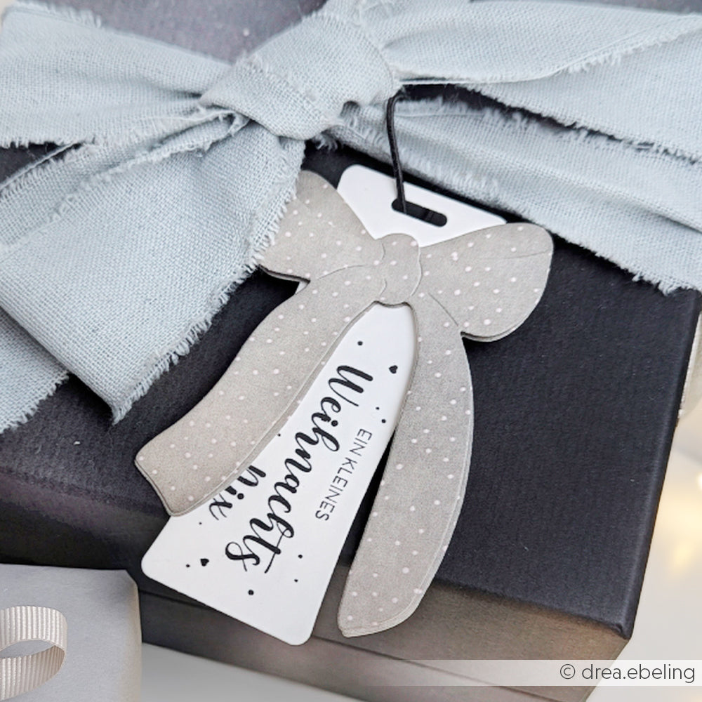 Geschenkverpackung aus grauem Stoff mit einer Schleife aus der Alexandra Renke Motivstanze Edelschleife mit der Aufschrift "Ein kleines Weihnachtsgeschenk".