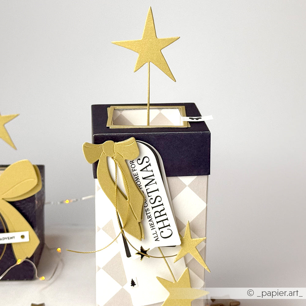 Geschenkschachtel mit goldenem Stern, goldener Schleife aus der Alexandra Renke Motivstanze Lieblingsschleife und einem Weihnachtsanhänger auf einfarbigem Hintergrund.