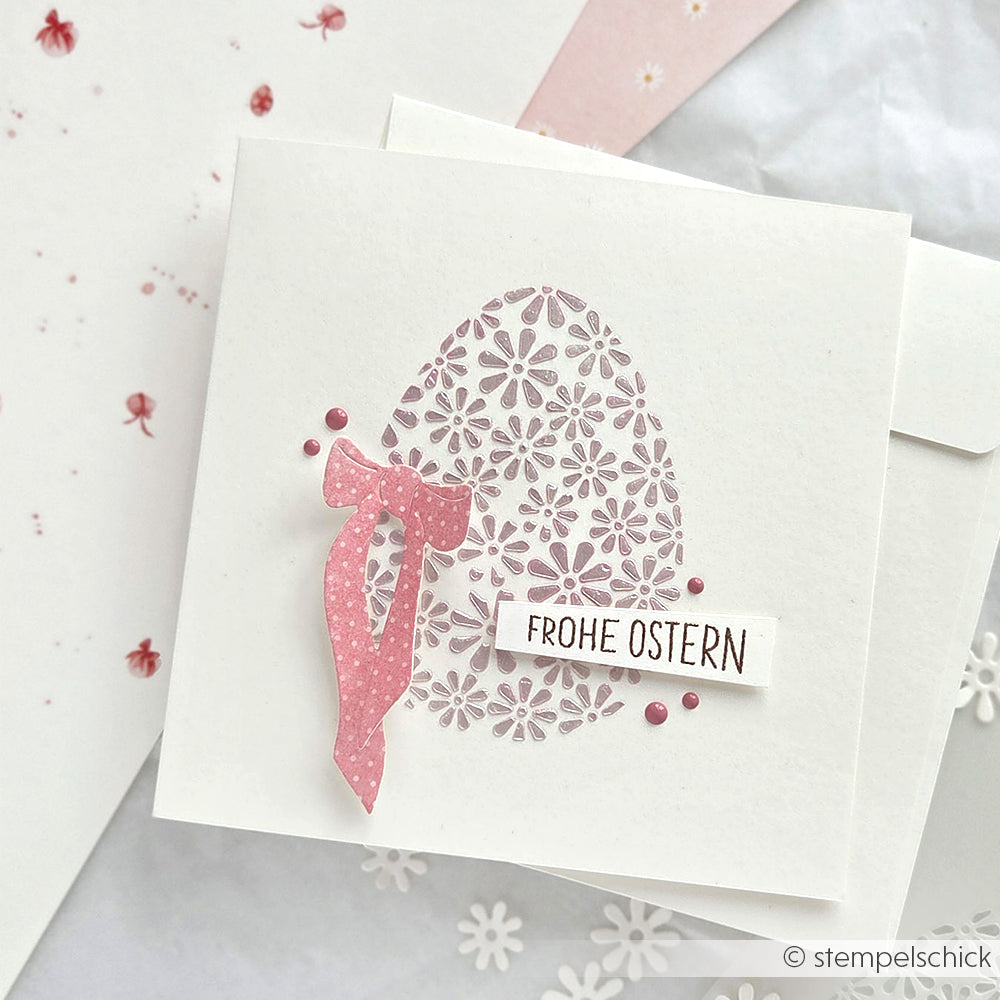 Quadratische Karte von Alexandra Renke mit einem geblümten Ei, einer rosa Schleife aus der Motivstanze Lieblingsschleife und dem Text "Frohe Ostern" auf weißem Hintergrund.