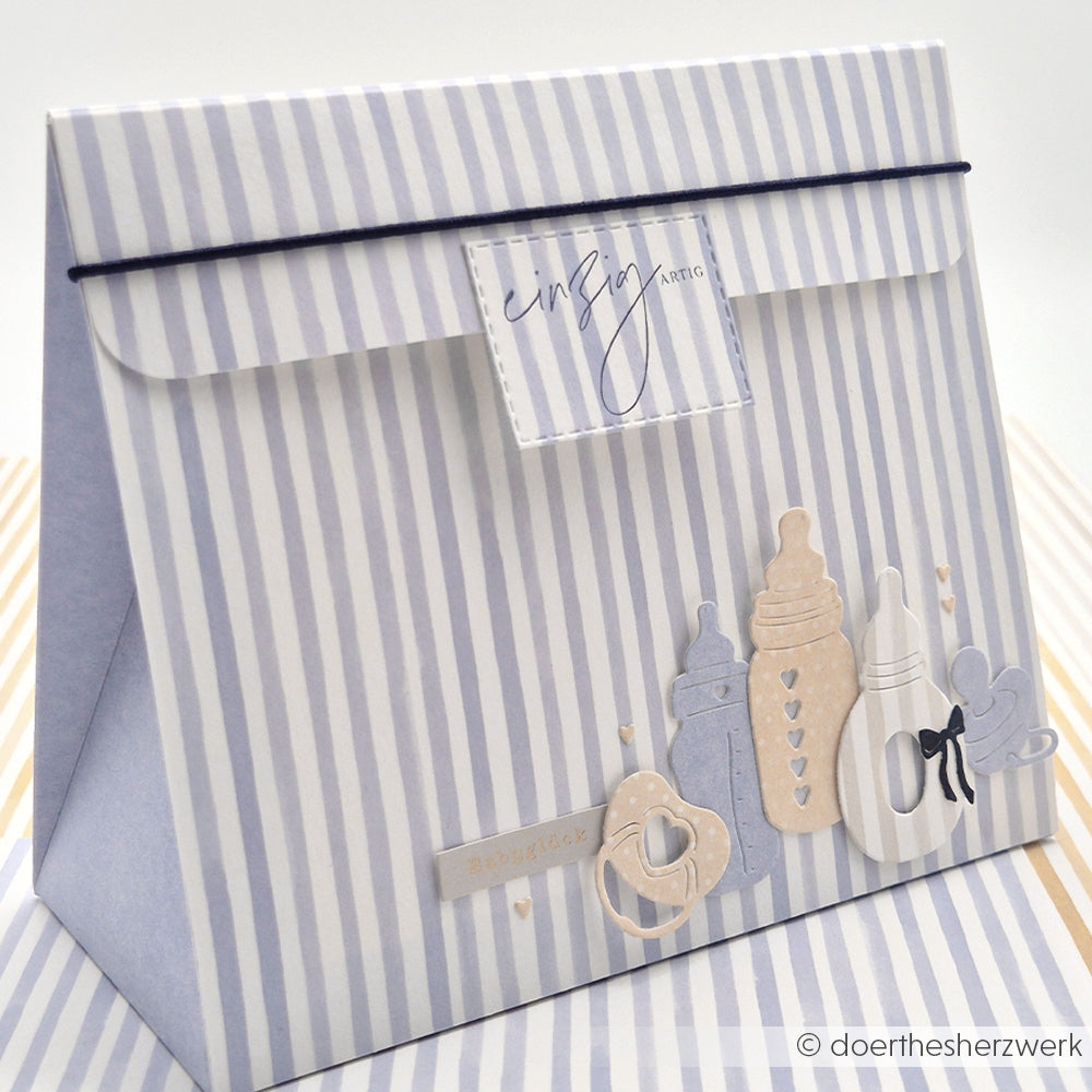 Gestreifte Geschenktasche mit Babyflaschen-, Schnuller- und Herzmotiven in zartem Blau und Beige, hergestellt mit dem Alexandra Renke Motivstanze Fläschchen Set für präzise Formen auf hochwertigem Designpapier.