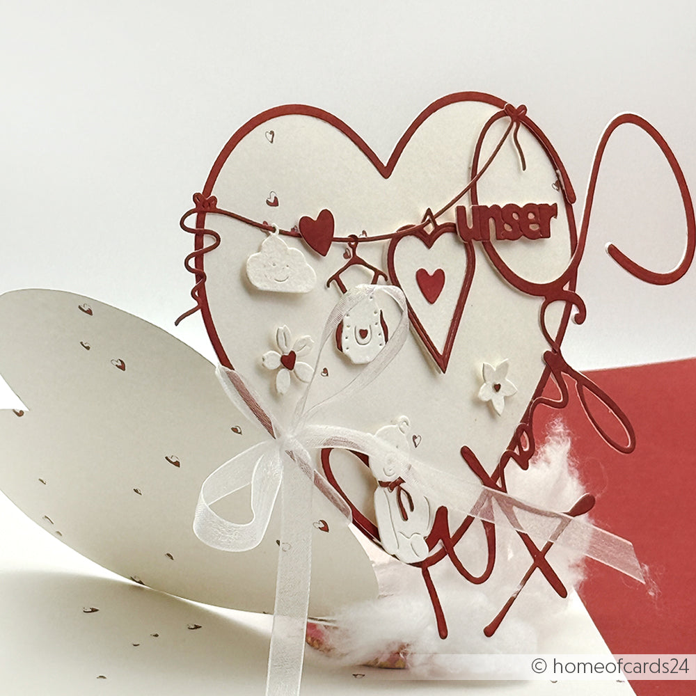 Handgefertigte Karte in Herzform von Alexandra Renke mit roten und weißen Akzenten, Schleifenband, hängenden Dekorationen und einer Motivstanze Herz sowie einem anpassbaren Text.