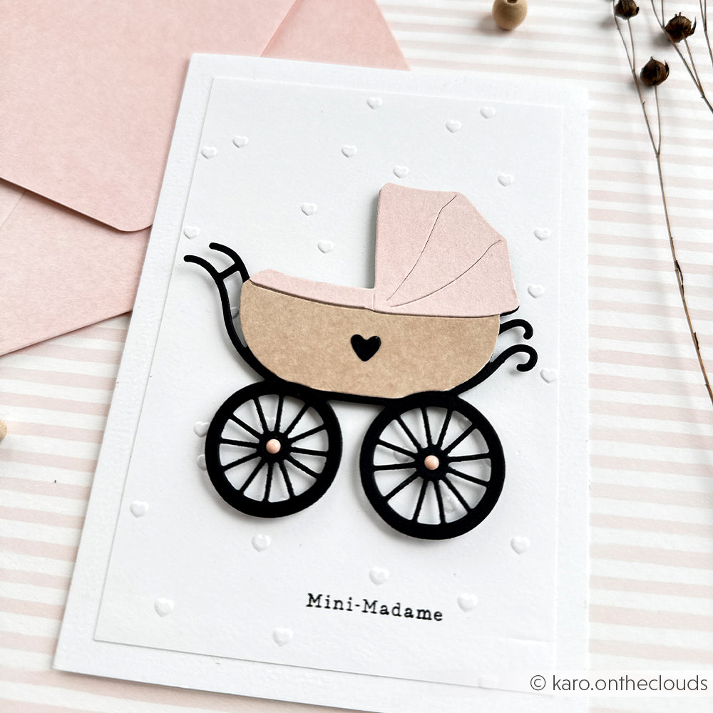 Grußkarte von Alexandra Renke mit einer Illustration eines rosa-beigen Kinderwagens, der mit der Motivstanze Kinderwagen und dem Text "Mini-Madame" am unteren Rand gestaltet ist.