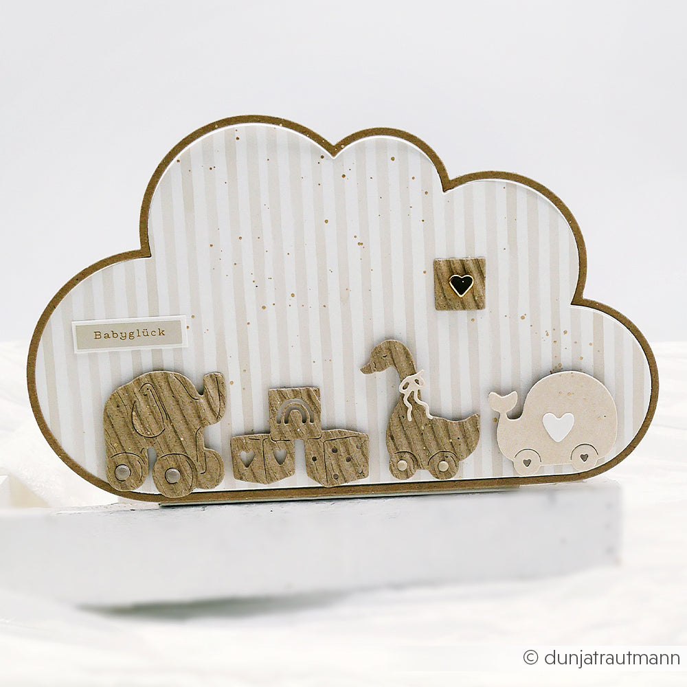 Mit Alexandra Renke Motivstanze Wolke gestaltete Karte in Wolkenform mit Holztierspielzeug, Bauklötzen und einem "Babyglück"-Aufkleber auf gestreiftem Hintergrund.