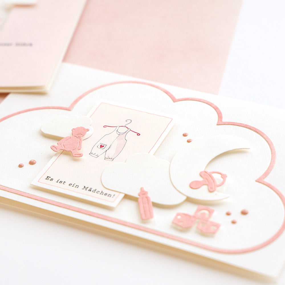 Karte mit Wolken, Babyartikeln und dem deutschen Text "Es ist ein Mädchen!" (in zarten Rosatönen. Eine charmante Kreation von Alexandra Renke Designpapiere und Motivstanze Kartenaufleger Wolke.