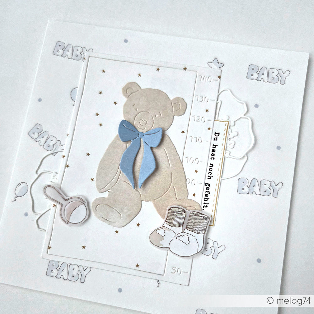 Handgemachte Babykarte von Alexandra Renke mit Teddybär, blauer Schleife, Babyschuhen, Söckchen, BABY-Textakzenten und eleganten Details aus Motivstanze und hochwertigem Designpapier.