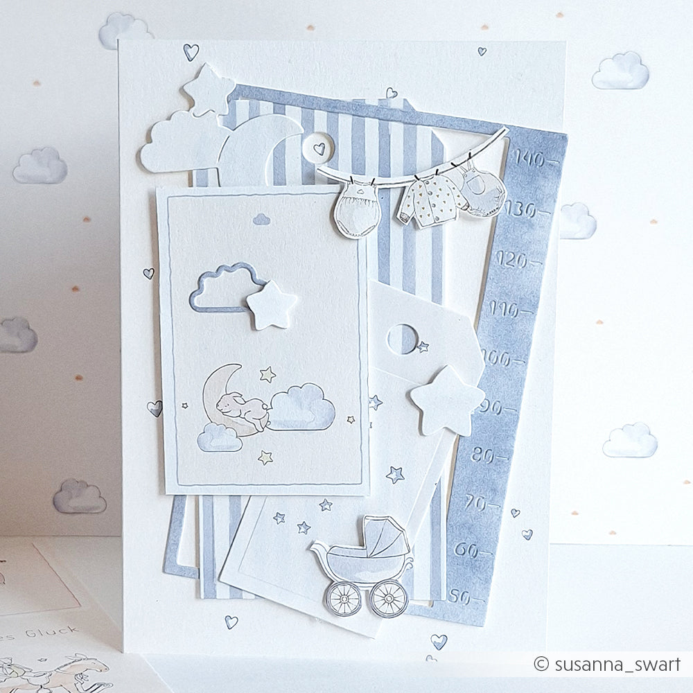 Handgemachte Babykarte von Alexandra Renke mit Wolken, Sternen, Babykleidung, Kinderwagen und weichen blau-weißen Schichten auf einem Wolkenhintergrund. Hergestellt mit Motivstanze für präzise ausgestanzte Details.