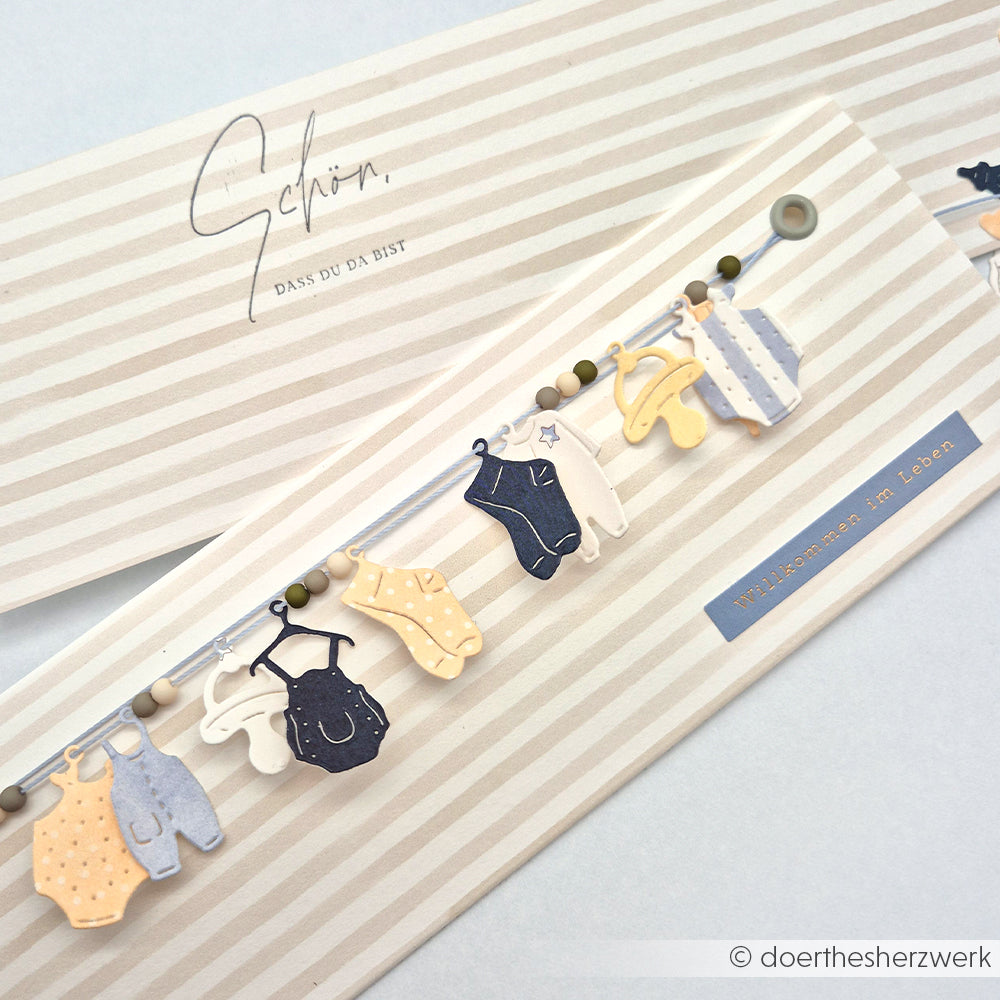 Grußkarte von Alexandra Renke mit Babykleidung an einer Schnur, hergestellt mit den Motivstanze Baby Anhänger Stanzen und elegantem Designpapier. Inklusive deutschem Text zur Begrüßung eines neuen Babys.