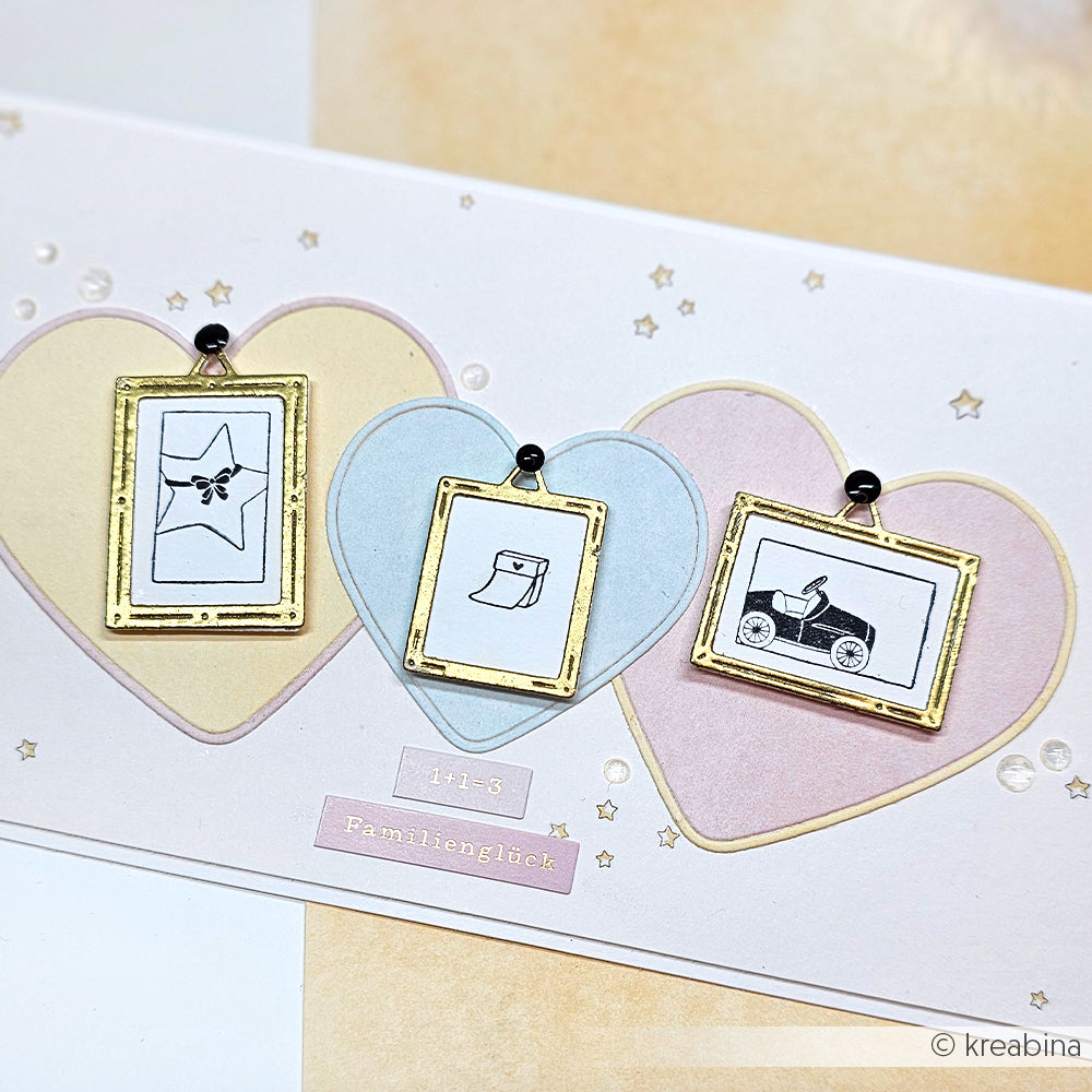 Drei goldgerahmte Charms auf pastellfarbenen Herzformen mit einfachen Baby-Zeichnungen - perfekt für Ihre Projekte mit Alexandra Renke Motivstanze Herzrahmen oder anderen DieCut Systemen.