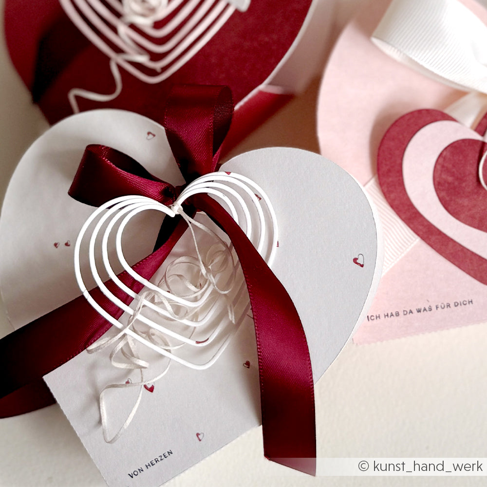 Weiße Herzkarten mit roten Schleifen und Herz-Akzenten, gestaltet mit Alexandra Renke's Motivstanze Herzrahmen und Stanzsystemen, arrangiert für einen romantischen Geschenkanlass und gestaltet mit elegantem Alexandra Renke Designpapier.