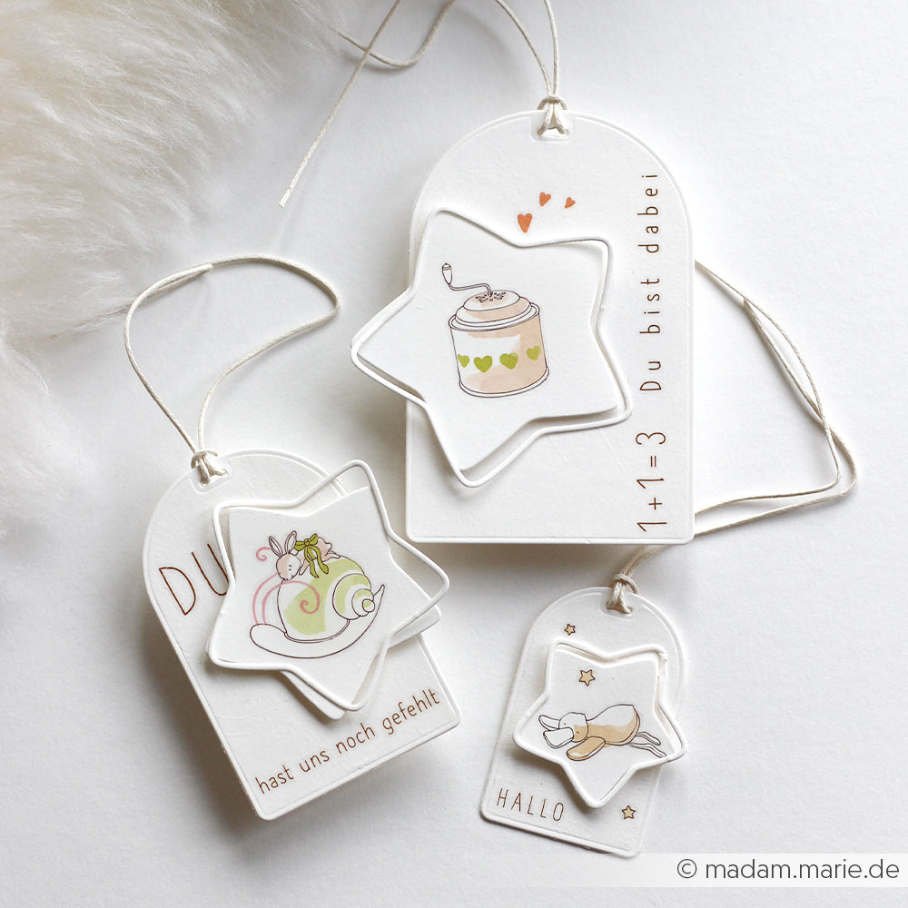 Drei weiße Geschenkanhänger von Alexandra Renke mit niedlichen pastellfarbenen Illustrationen und deutschen Sprüchen, jeweils mit einer weißen Schnur. Ideal zum Kombinieren mit Designpapieren oder zum Aufwerten von Geschenken, die mit DieCut Systemen hergestellt wurden.