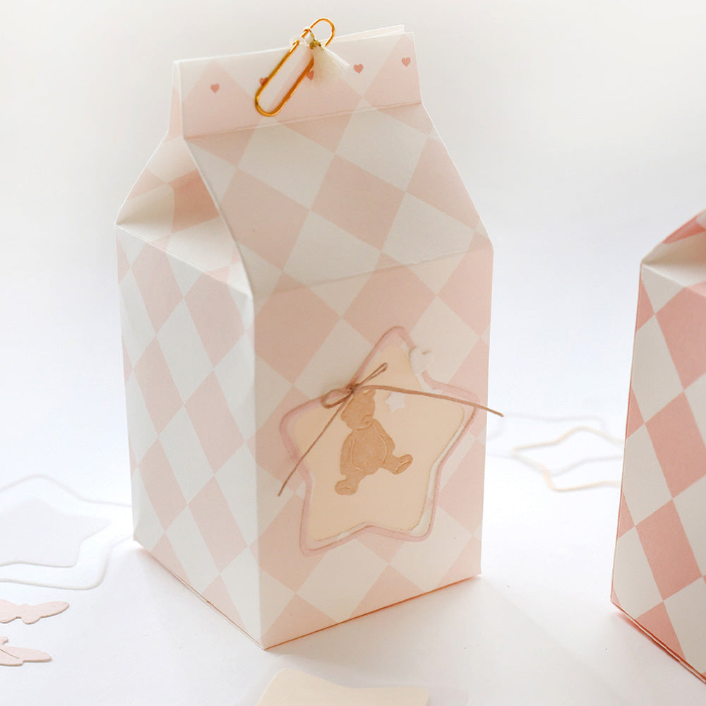 Die rosa-weiß karierte Milchkartonschachtel von Alexandra Renke aus hochwertigem Designpapier hat einen mit Schnur gebundenen Bärenanhänger, eine goldene Büroklammer auf der Oberseite und ist mit der Motivstanze 5 Sternrahmen verziert, die für zusätzlichen Charme sorgt.