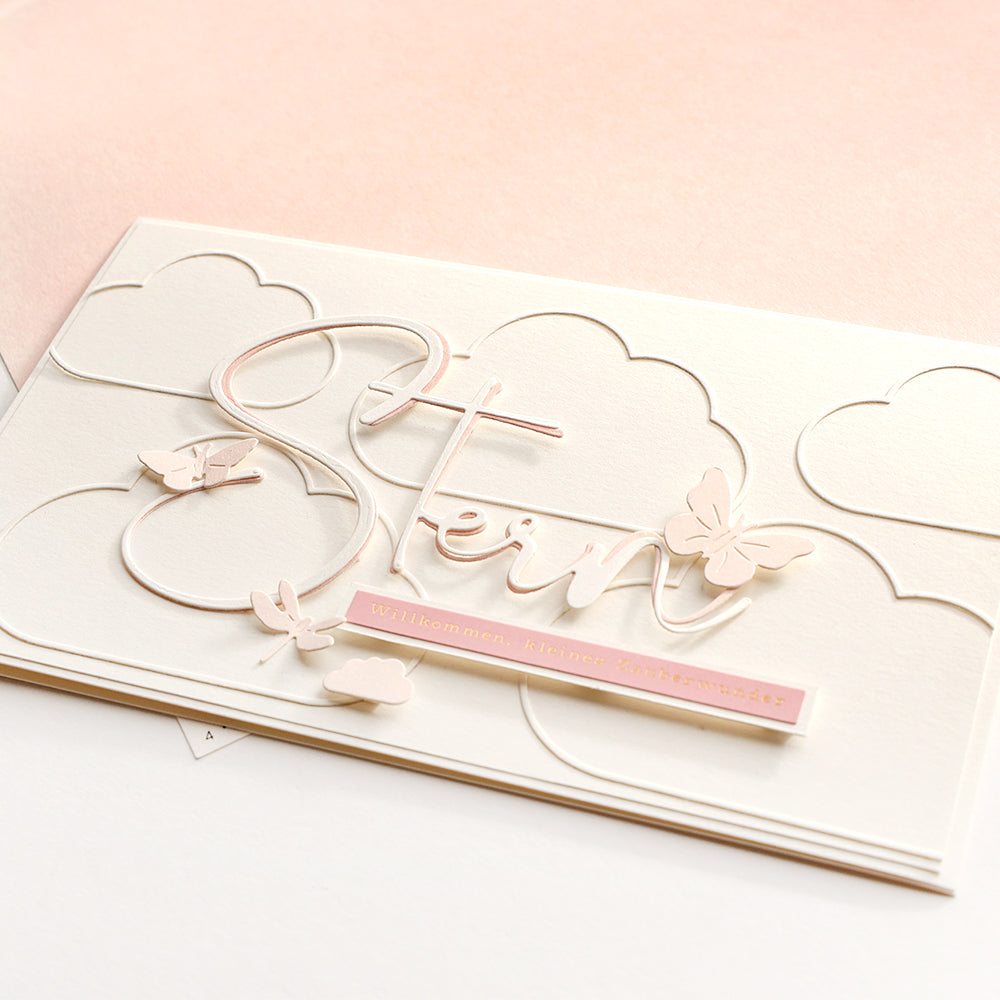 Elegante Karte von Alexandra Renke mit "Stern", Schmetterlingsausschnitten aus Motivstanze und Wolkenmotiven auf rosa-weißem Wolkenrahmen-Hintergrund.