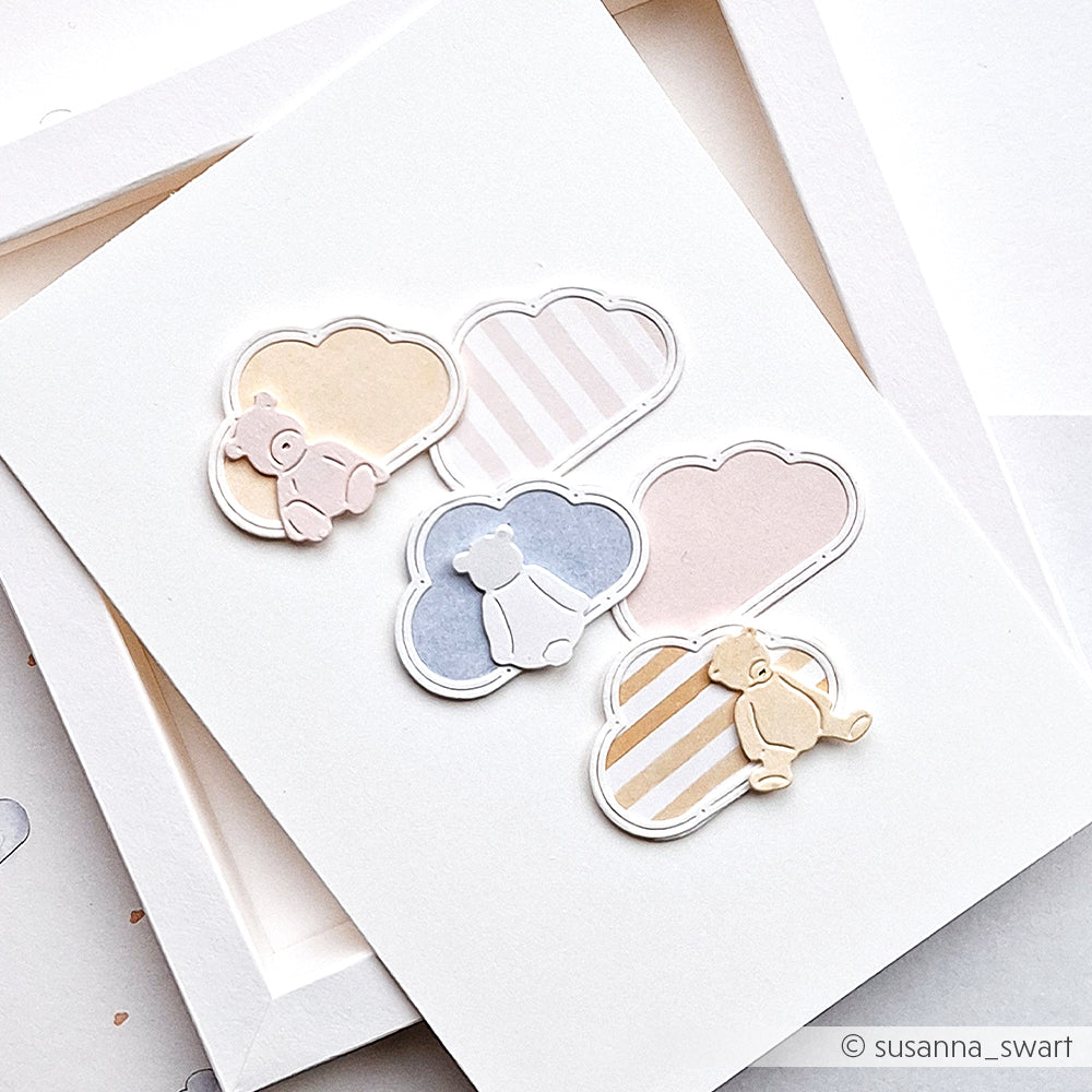 Grußkarte von Alexandra Renke mit pastellfarbenen Wolken, Streifen und drei ausgeschnittenen Teddybären in Beige, Blau und Creme. Mit einem bezaubernden Wolkenrahmen, der mit präziser Motivstanze gefertigt wurde und eine ganz besondere Note hat.