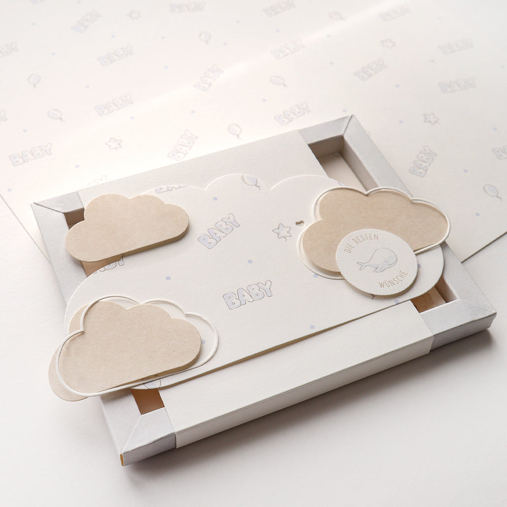 Eine Grußkarte zum Thema Baby mit beigen Wolkenausschnitten, die mit der Alexandra Renke Motivstanze Wolkenrahmen und dem Text BABY gestaltet sind, präsentiert in einer Geschenkbox.