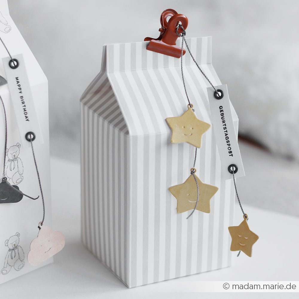 Eine gestreifte Geschenkbox mit roter Klammer, 3 Sterne mit Ösen aus einer Motivstanze und ein Geburtstagspost-Etikett von Alexandra Renke zum Aufhängen.