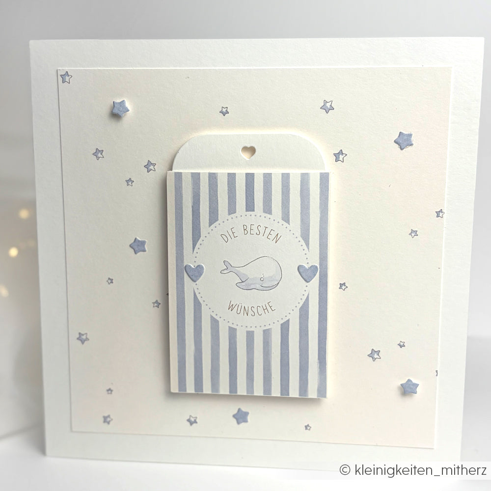Alexandra Renke Karte: Quadratisch, blaue Streifen, Sterne, Herzen, Wal-Illustration und "Die besten Wünsche" auf Deutsch. Ein charmantes Motivstanze-Detail und ein Etikett im Tütchen-Herz sorgen für einen verspielten Abschluss.