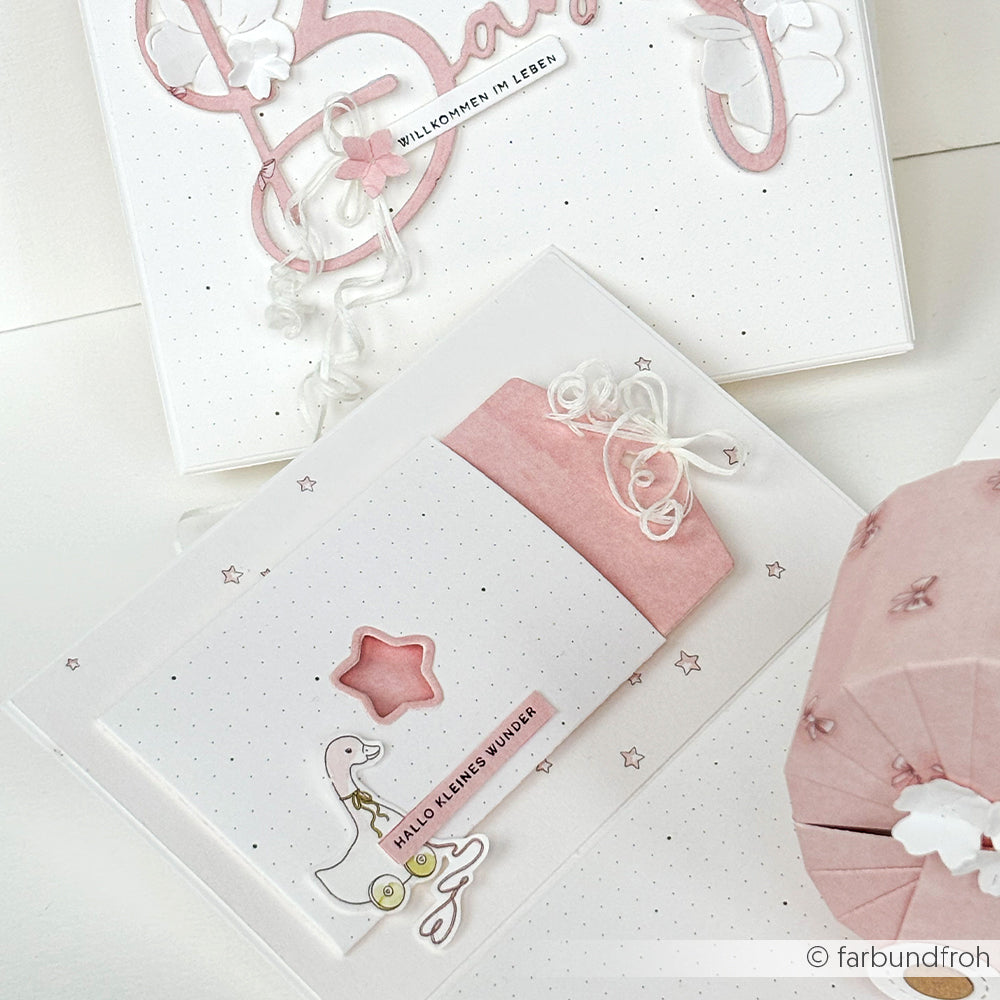 Alexandra Renke Grußkarte mit rosa und weißer Baby-Dekoration, Kinderwagen, Stern und deutschem Text. Eine Motivstanze mit Etikett im Tütchen-Stern sorgt für zusätzlichen Charme.