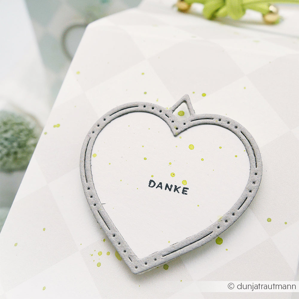 Weiße Geschenkschachtel von Alexandra Renke mit einem herzförmigen Motivstanze Herz-Rähmchen-Anhänger mit "DANKE" und kleinen grünen Farbspritzern.