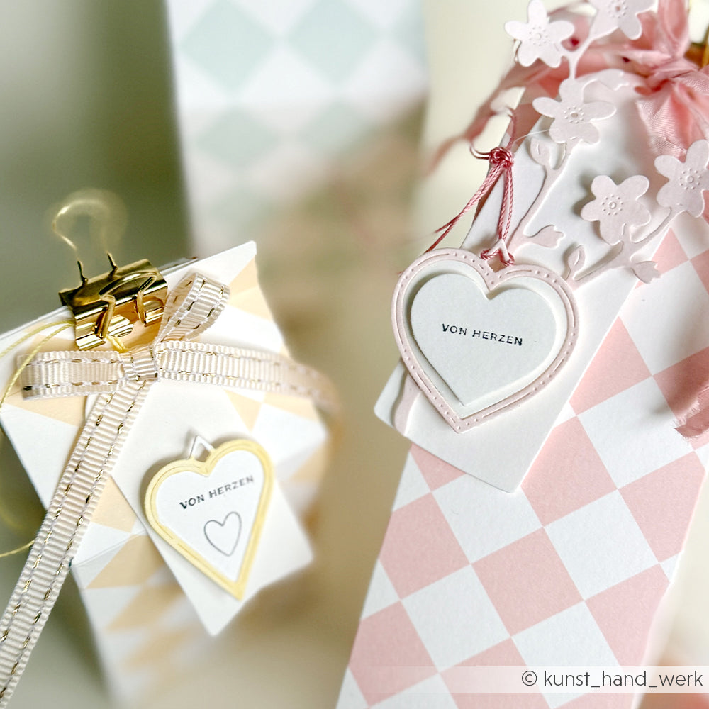 Geschenkschachteln mit pastellfarbenen Rautenmustern von Alexandra Renke, verziert mit herzförmigen Anhängern aus der Motivstanze Herz-Rähmchen, dazu zarte Bänder und Blumenschmuck.