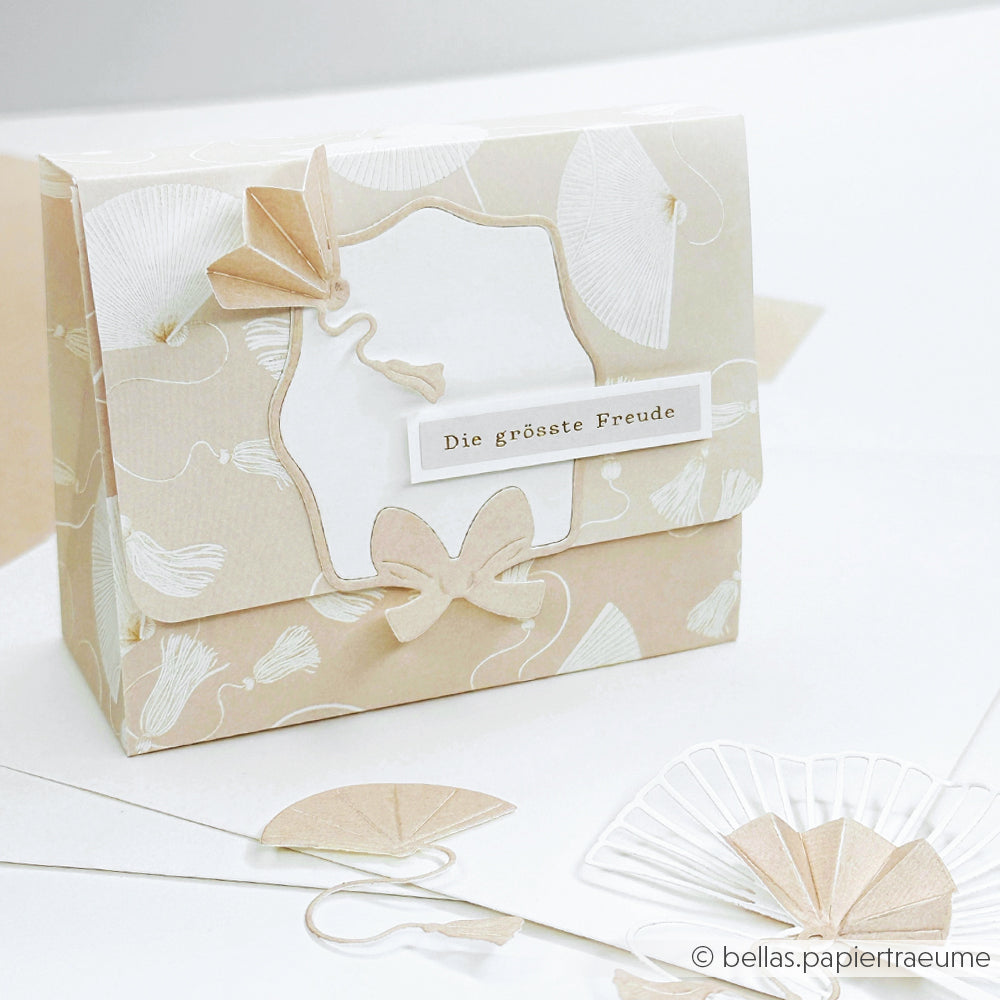 Eine handgefertigte beige-weiße Geschenkbox von Alexandra Renke mit einem Schmetterlings- und Blumendesign mit der Aufschrift "Die größte Freude" wird durch einen eleganten Vintage-Rahmen akzentuiert, der mit filigranen Stanzsystemen gefertigt wurde und zusätzlichen Charme versprüht.