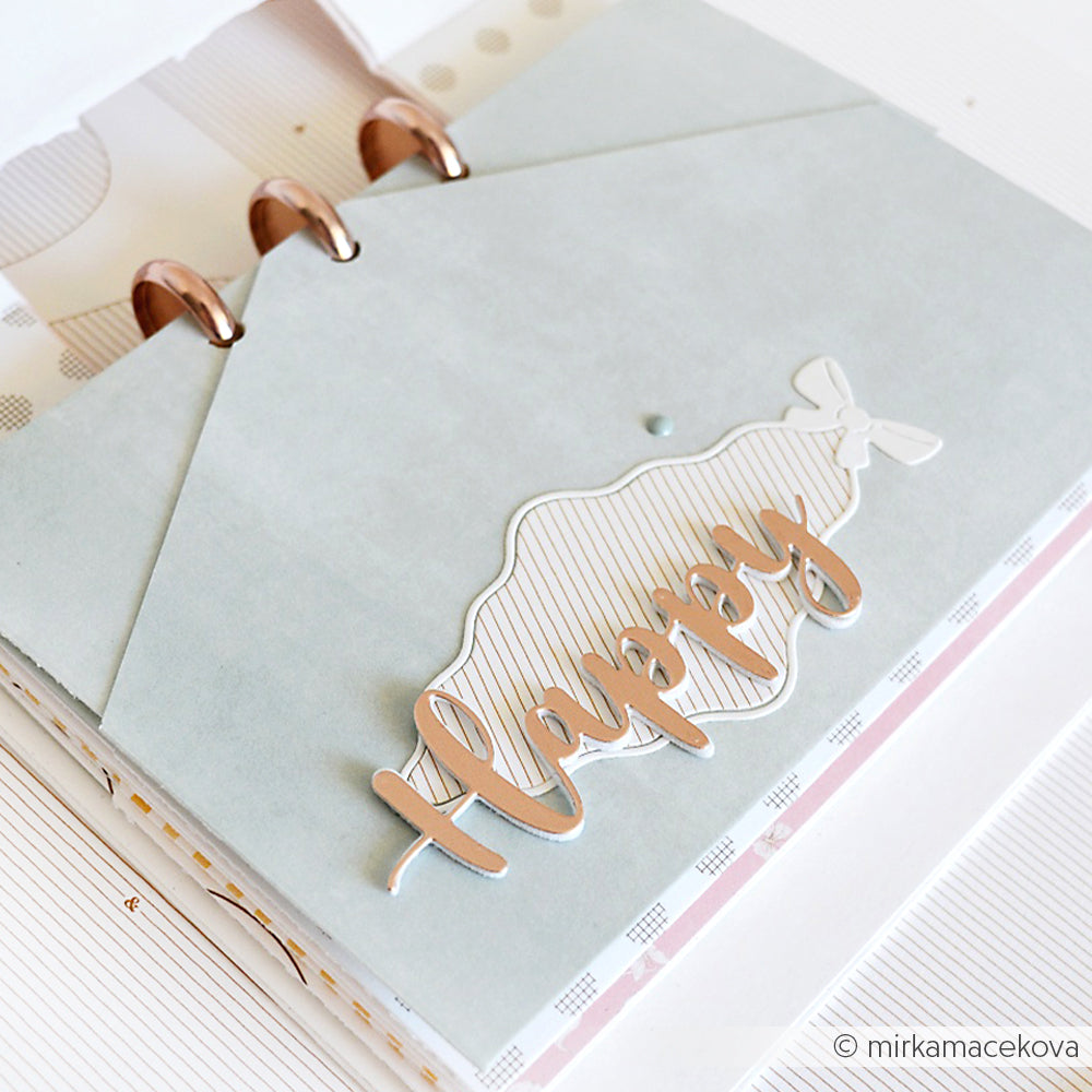 Eine Scrapbook-Seite mit einem dekorativen Umschlag, "Happy" in Metallic-Schrift und Akzenten, die mit Alexandra Renke Dies für Designpapier wie der Motivstanze geschwungener Rauten-Rahmen gemacht wurden.